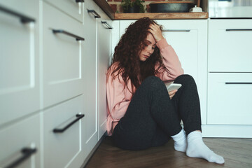 Young caucasian woman using mobile phone on kitchen floor