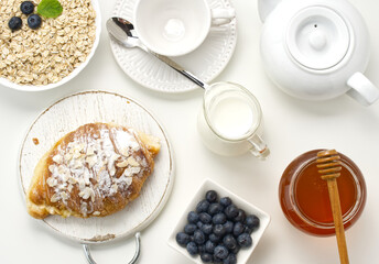 Obraz na płótnie Canvas Raw oatmeal in white ceramic plate, blueberry, honey on white table, breakfast