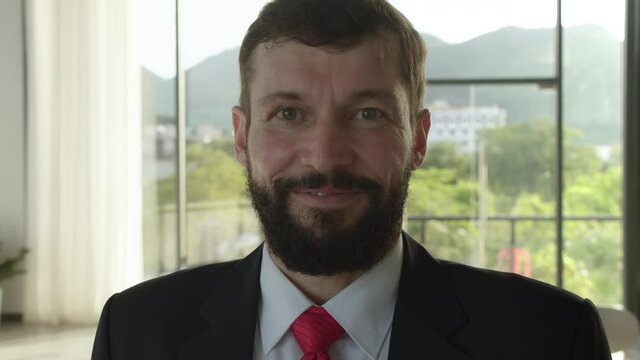 Close up of cheerful male boss with beard looking to camera and smiling. Good looking caucasian man team leader in modern company office. Portraits. Concept of people and emotions.