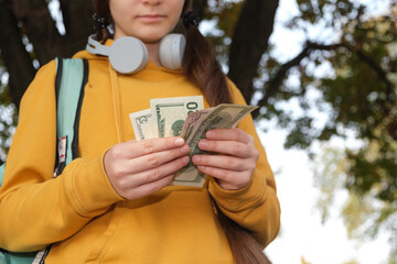 A teenage girl in headphones counts dollar bills, pocket money