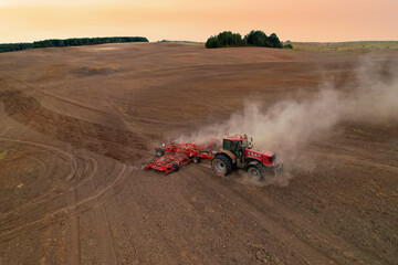 Obraz premium Tractor on cultivating field work. Soil Tillage in farmers country. Agricultural tractor on cultivation field for sowing seeds. Farming and seeding concept. Planting Equipment and Farm Machine.