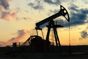 Crude oil pump jack at oilfield on sunset backround. Fossil crude output and fuels oil production. Oil drill rig and drilling derrick. Global crude oil Prices, energy, petroleum demand