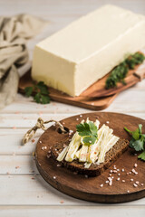 Soft and fresh butter slices spread on black bread with fresh herbs on a wooden board.