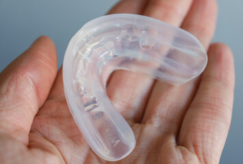 transparent mouth guard made of silicone, for straightening teeth in children, in a girl's hand, in daylight. Hygiene, dental care, occlusion correction, new technologies