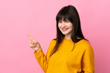 Young Ukrainian woman isolated on pink background pointing finger to the side and presenting a product