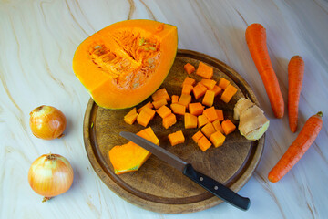 Autumn dishes, pumpkin soup cooking. pumpkin is cut on the kitchen table on a wooden board, next to onions, carrots and ginger