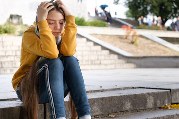 Sad teenage girl in headphones will cover her face with her hands, a place for text