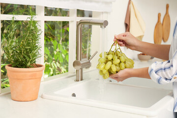 Woman washing grapes under tap water in kitchen sink, closeup