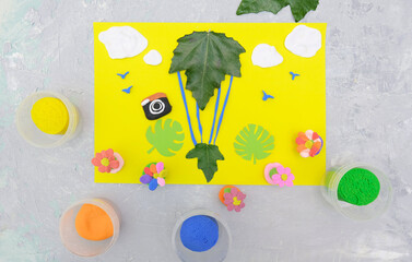 Child making card from paper, plasticine and natural leaves. Air balloon, clouds, birds, flowers... Inspiration for children. Plasticine and paper art children project. Travel holiday concept