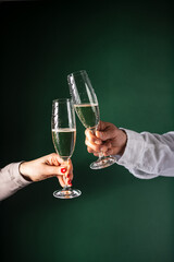 Male and female hands holding and clinking champagne glasses with champagne on green background