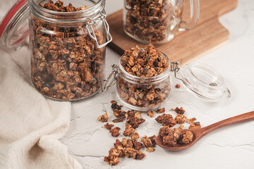 Mason jar with granola breakfast cereal with nuts. wooden spoon with scattered granola in front and...