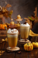 Two glasses of an orange pumpkin spice latte coffee drink with whipped cream, brass drinking straw and cinnamon sprinkles