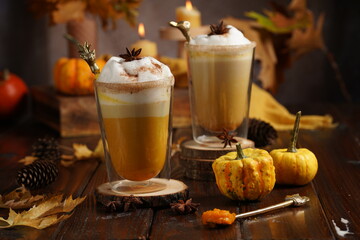 Two glasses of an orange pumpkin spice latte coffee drink with whipped cream, brass drinking straw...