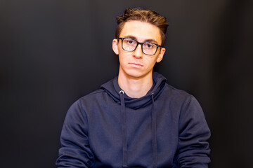 young man serious thinking with dark sweatshirt on dark background. Beautiful student with glasses