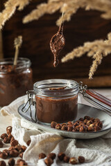Homemade hazelnut cocoa chocolate cream in mason jar on plate surrounded by hazelnuts