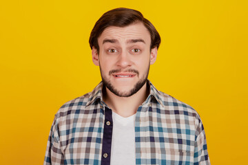 Close up photo of youn gman bite lips teeth worried fail problem checkered shirt outfit isolated yellow bright background