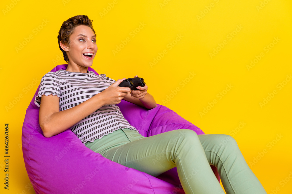 Wall mural Photo of optimistic young lady sit play station look empty space wear t-shirt jeans isolated on yellow background