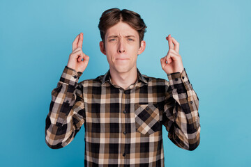Photo of young guy worried nervous crossed fingers beg wish luck success isolated on blue color...