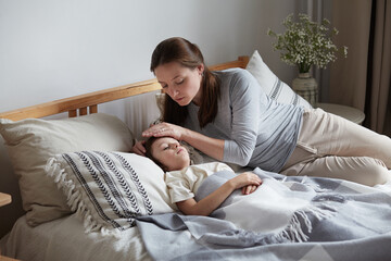 Mother worried son health check hot forehead lying on bed pillow. Unhappy preschooler feeling head pain ache virus disease at home. Female babysitter taking care male kid. Child boy have fever symptom