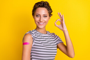 Photo of cool young brown hairdo lady show okey vaccinated wear white t-shirt isolated on yellow...