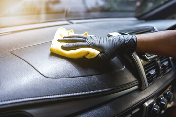 Technician with gloves cleaning the car dashboard with red cloth. Topical car wash and care.