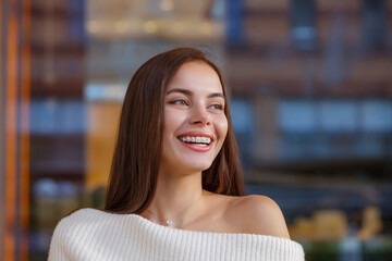 Emotional portrait of a beautiful happy smiling young woman with braces. girl with bracket system posing in city outdoor. Brace, bracket, dental care, malocclusion, orthodontic health concept, blurred - obrazy, fototapety, plakaty