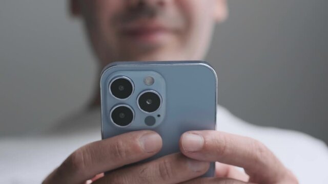 New Iphone 13 Pro in Sierra Blue Color. Latest 2021 Apple smart phone model filmed in close up. Young man browsing messages on of screen with smile