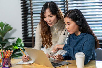 Asian colleague, female marketer Standing and chatting with girls typing laptops, helping to create ideas at the office desk at the company. 