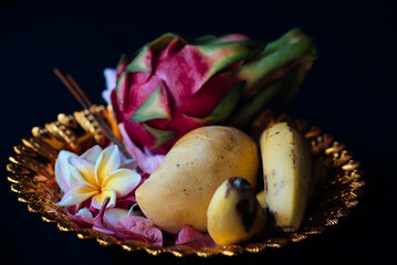 offering to buddha in golden plate with dragon fruit, mango, banana and plumeria flower