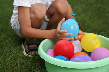 Fototapeta na wymiar Little boy with basin of water bombs on green grass, closeup