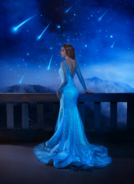 Photo with noise. Fantasy woman princess stands on balcony looks at night sky space cosmos falling stars. Girl enjoy magic starfall ball. Elegant long shiny blue evening dress . Fairy lady Queen