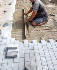 A worker lays down sand for paving slabs.