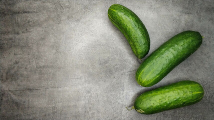 Three fresh green cucumbers on gray marble background.