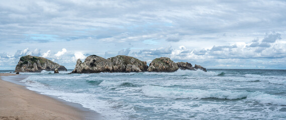 Beautiful sandy ocean beach with large rocks on the shore and in the water. Powerful waves on ocean. Ocean water splash on rock beach with Rugged cliffs. panorama