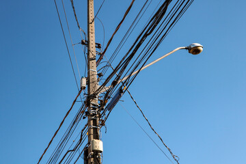 Public lighting electric network pole with a tangle of wires, with the lamp rod and the blue sky in...