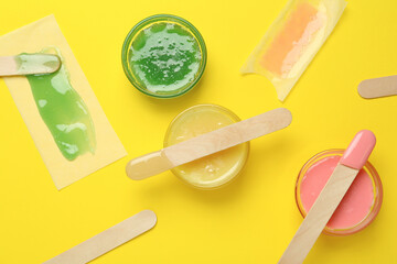 Flat lay composition with different types of wax and spatulas on yellow background