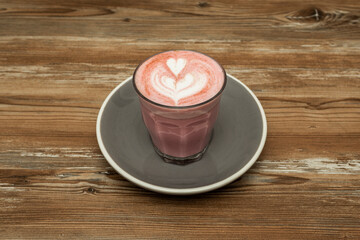 Pink latte served by a barista who draws hearts on wooden table