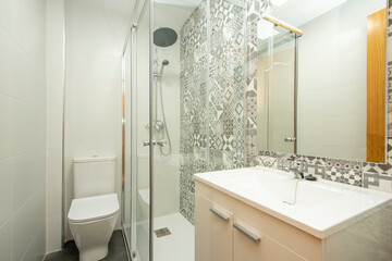 Bathroom with white cabinets, shower with large shower head and hydraulic tiles on the wall
