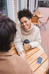 happy african american woman holding hands with blurred boyfriend near smartphone and paper cup.