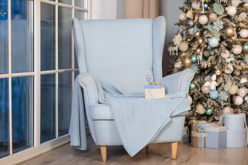 Christmas interior decoration. Gift box on armchair near christmas tree.