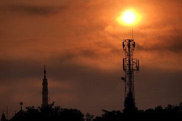 mosque minaret and communication tower during sunrise. radio frequency transmission tower