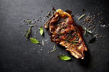 Juicy beef steak with herbs and spices on black slate background. Copy space