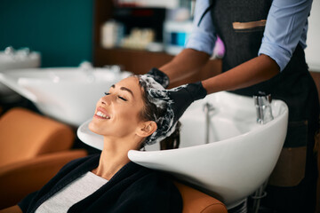 Young woman enjoys while getting her hair washed at hairdresser's.