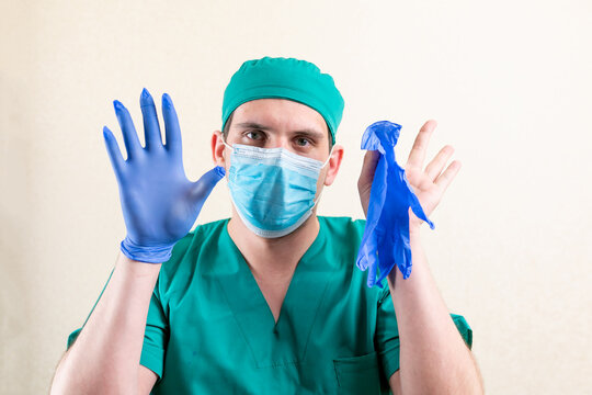 A doctor in a mask and a cap, plays with gloves.
