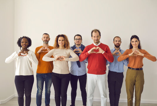 Team of happy multiracial youth and old citizens sending you love, support and gratitude. Studio group portrait of thankful young and mature people standing together and doing heart shape hand gesture