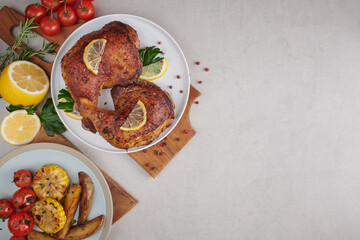 Grilled chicken legs in barbecue sauce and roasted vegetables with tomatoes, pepper seeds, salt in wooden cutting board on light color  stone table. Top view, copy space. Tasty snack . Flat lay.