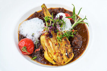 Game stew with roasted fennel vegetables, tomatoes and decorative foam, garnish of cress, herbs and sprouts, served in a deep white plate, copy space, selected focus