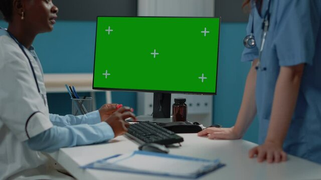 Close up of computer with horizontal green screen on desk while doctor and nurse talking. Medical team using monitor with mockup template and isolated background for chroma key.