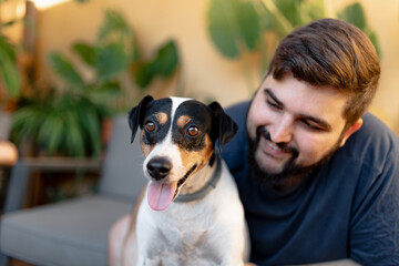 Friendly young man hugging his cute grocer dog with both hands and looking at camera. The dog has the tongue out and is looking away/