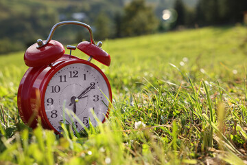 Red alarm clock on green meadow in morning